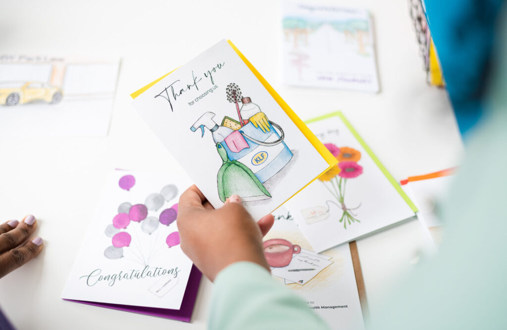 Hand picking up a "Thank You for Choosing Us Cards" or "Thank You for Your Purchase Cards" corporate greeting card from a selection of custom company greeting cards.